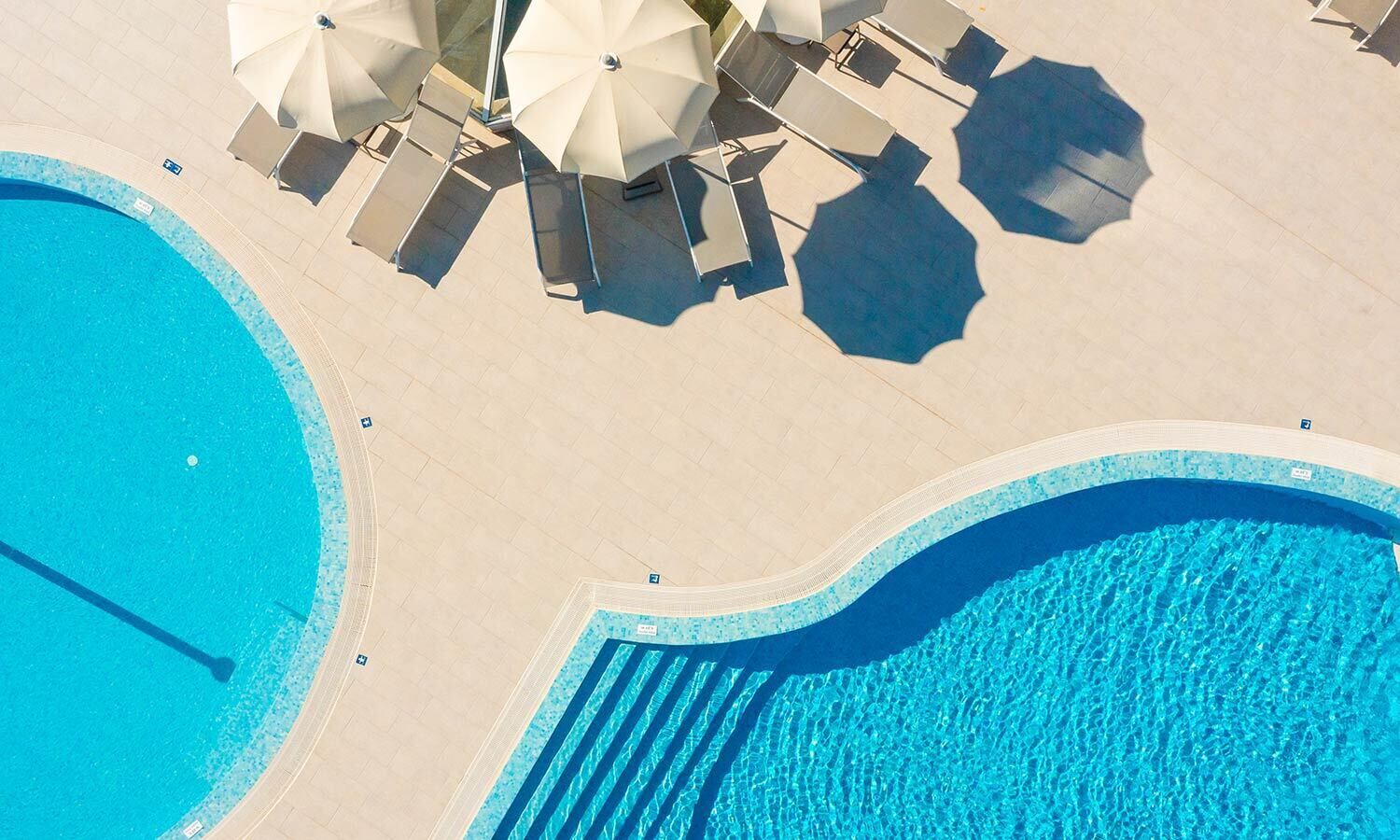 An aerial view of a pool area with two distinct swimming pools, sun loungers, and umbrellas.