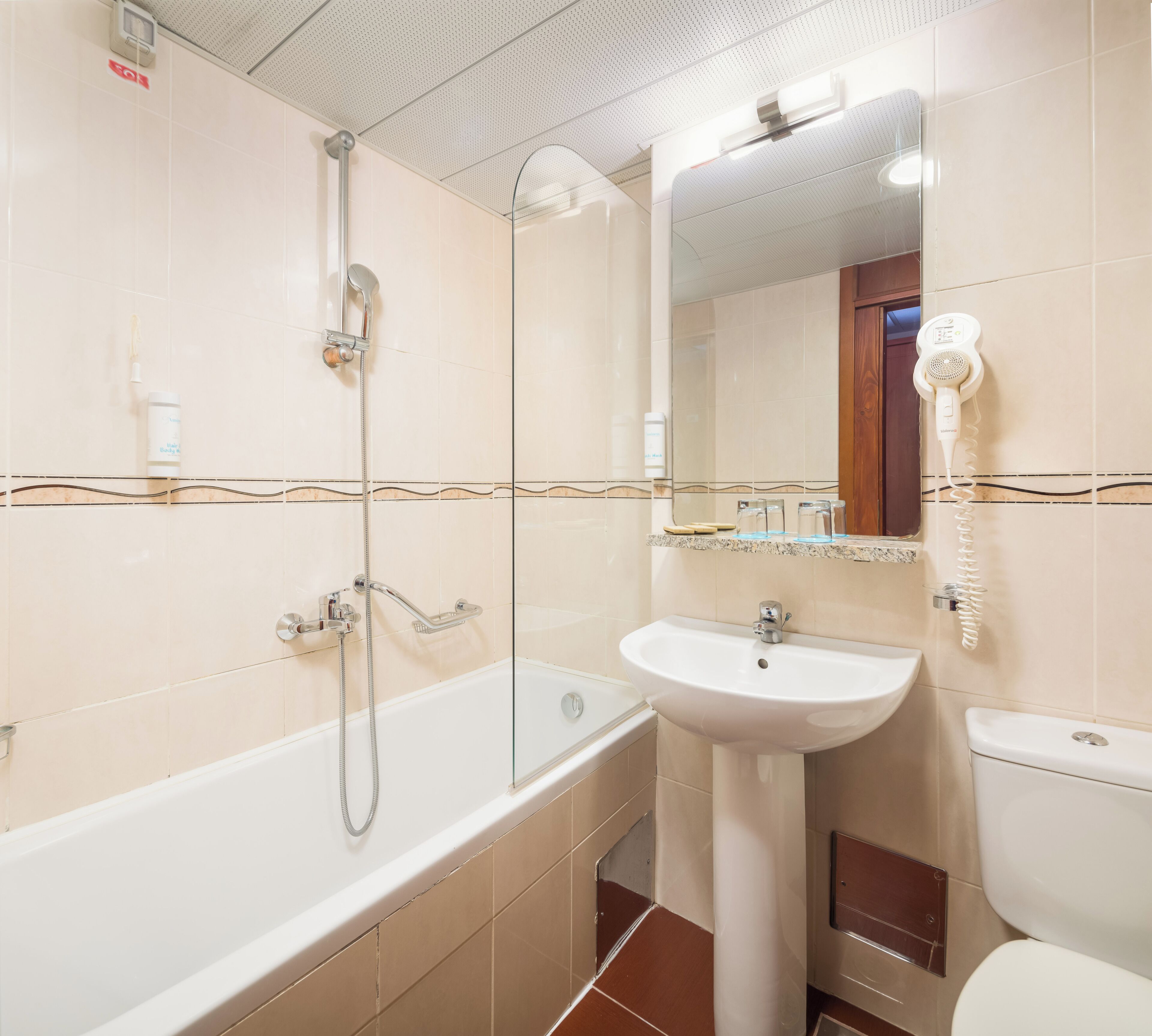 Un baño con bañera, lavamanos, inodoro y secador de pelo montado en la pared.