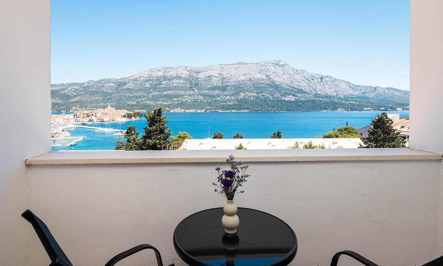 Un balcon offrant une vue sur une ville côtière, une chaîne de montagnes et une mer bleue et limpide.