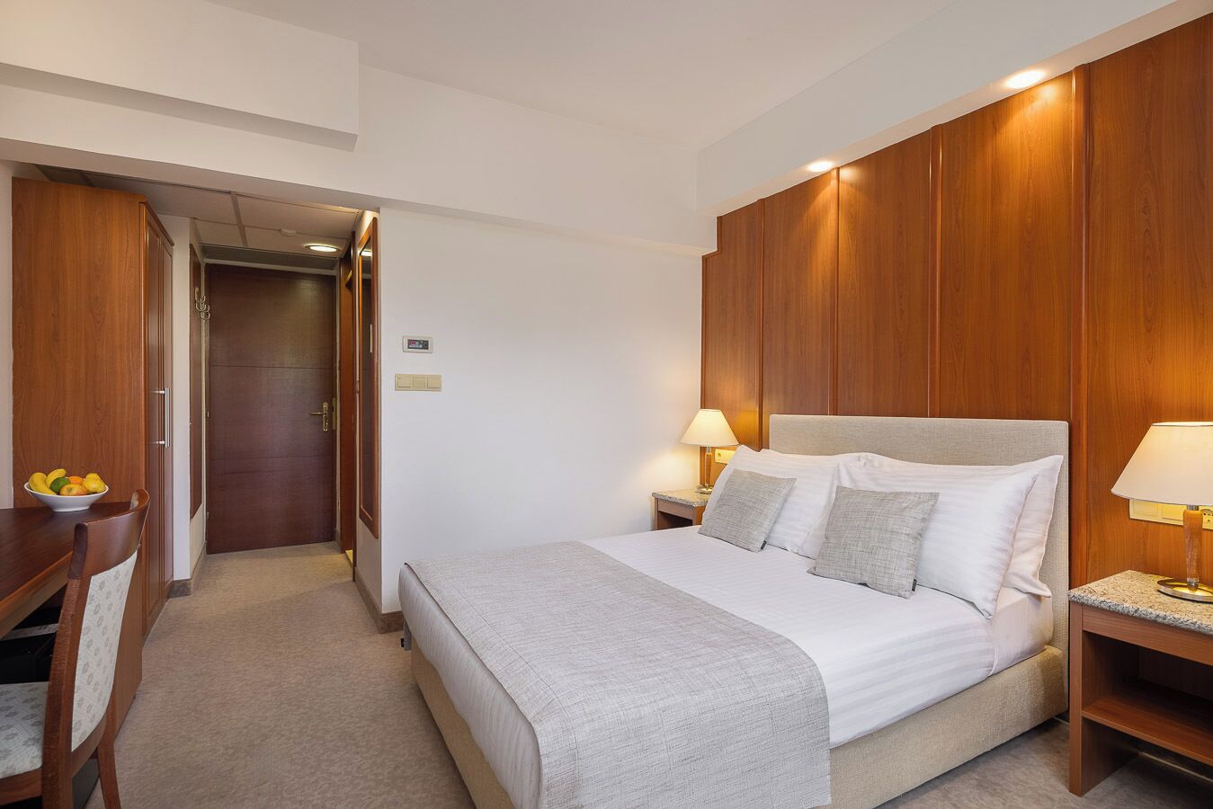 A hotel room with a bed, bedside tables, a desk, and a wardrobe.