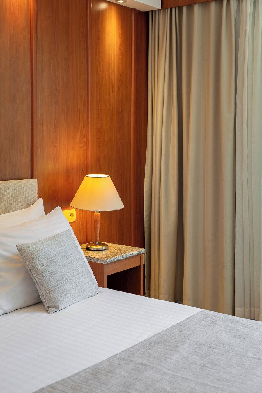 A hotel room with a bed, a nightstand, a lamp, and curtains.