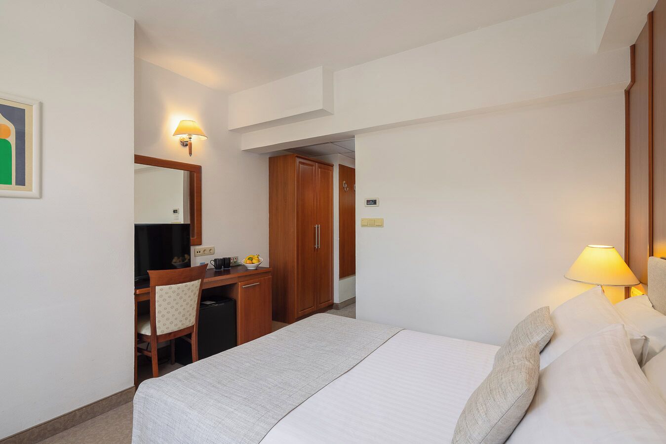 Una habitación de hotel con cama, escritorio, silla y armario.