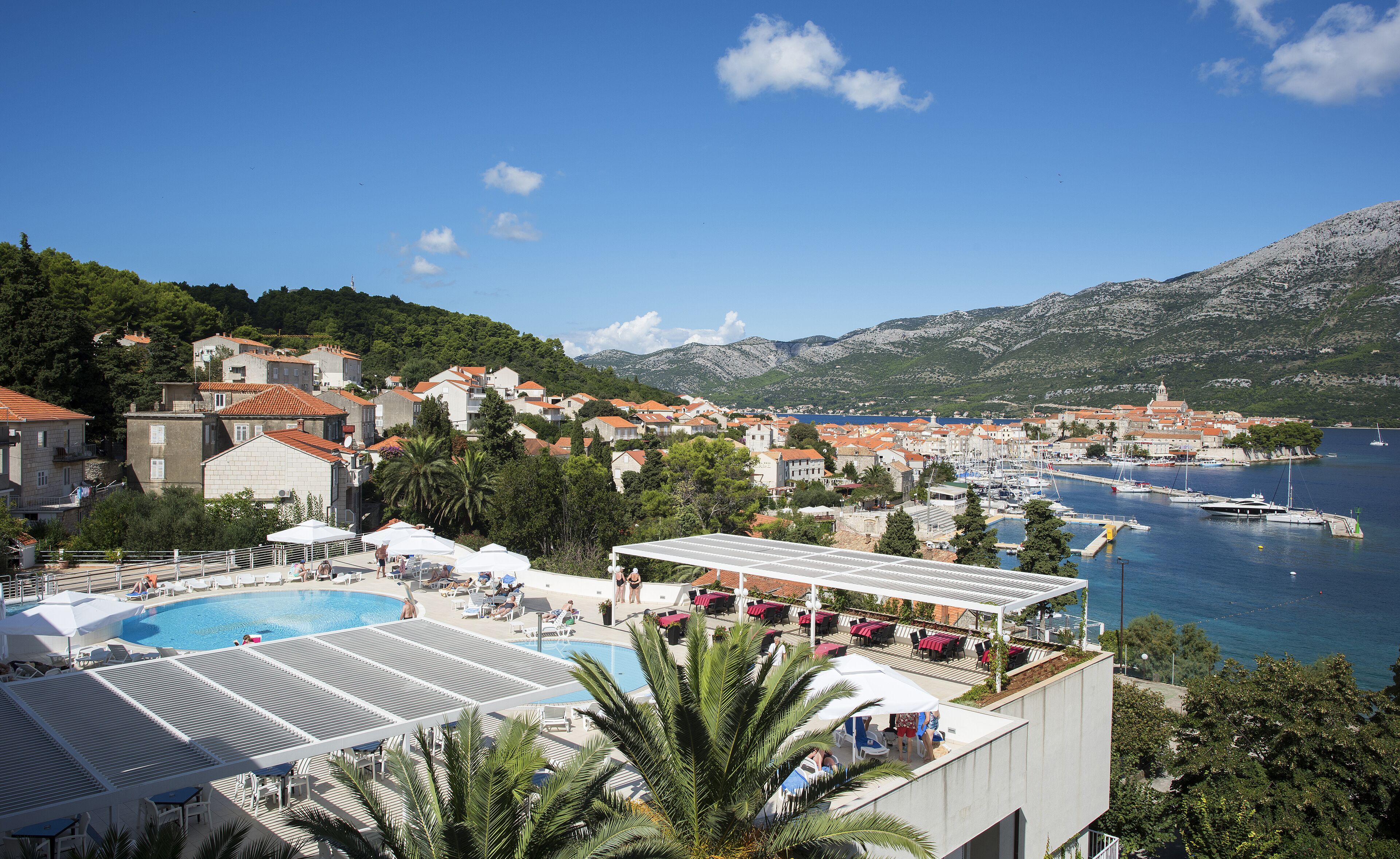 Um resort à beira-mar com piscina, espreguiçadeiras e vista para o mar e montanhas.