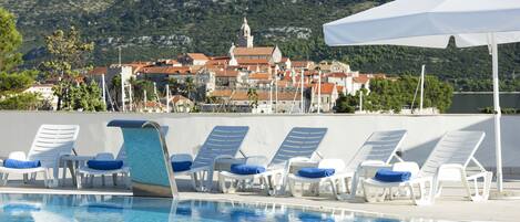 A pool area with lounge chairs and a view of a town with historic buildings.