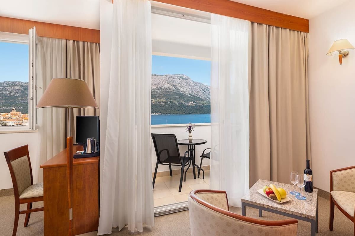 Een hotelkamer met balkon, een tafel met fruit en een fles, en een televisie op een bureau.