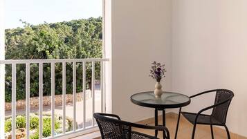 A balcony with a table and chairs, a vase with flowers, and a view of a green landscape.