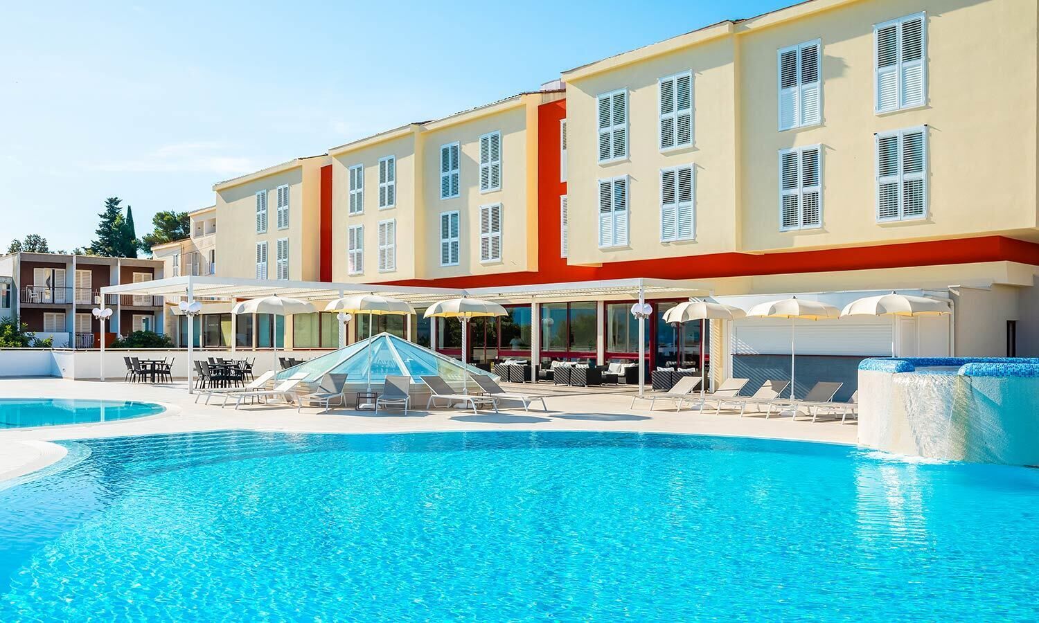 A hotel with a swimming pool, outdoor seating, and a covered area.