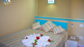 Habitación de hotel con cama, ropa de cama a rayas, toalla blanca con rosas, teléfono y una lámpara fijada a la pared.