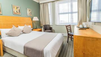 A hotel room with a large bed, a desk, a chair, a lamp, and a window with curtains.