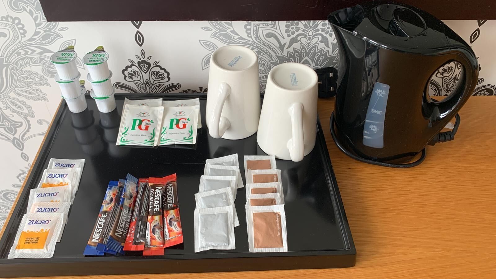 A tray with coffee-making supplies, including Nescafé capsules, PG coffee packets, Zucro sweetener packets, and a coffee maker.