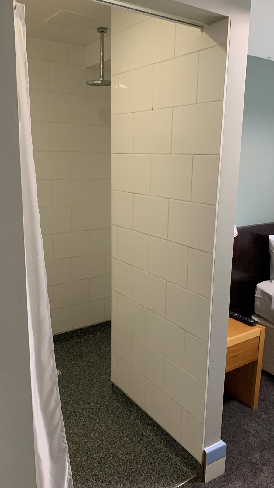 Un baño con paredes de azulejos blancos, una zona de ducha y un banco de madera.