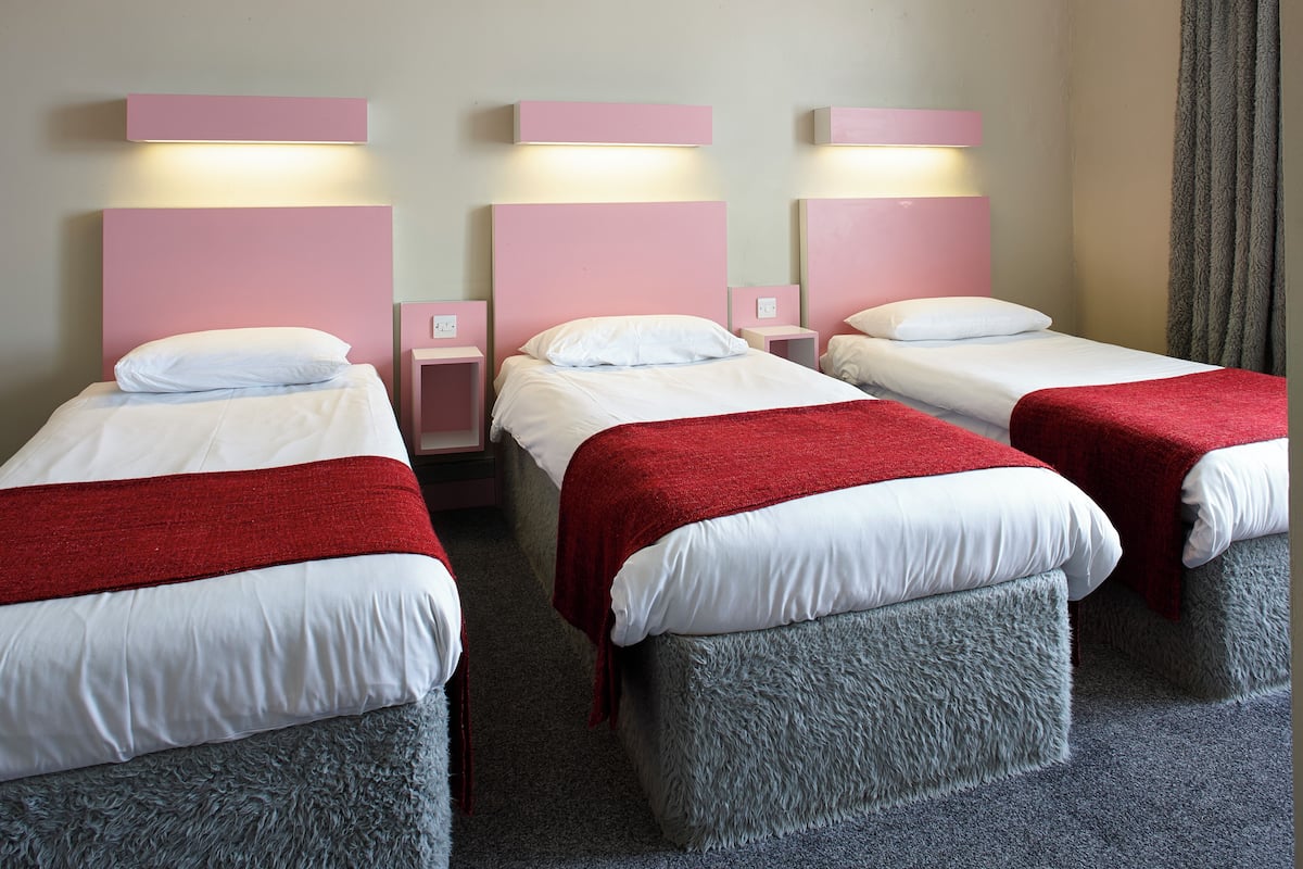 A hotel room with three beds, each with a red blanket and white bedding.
