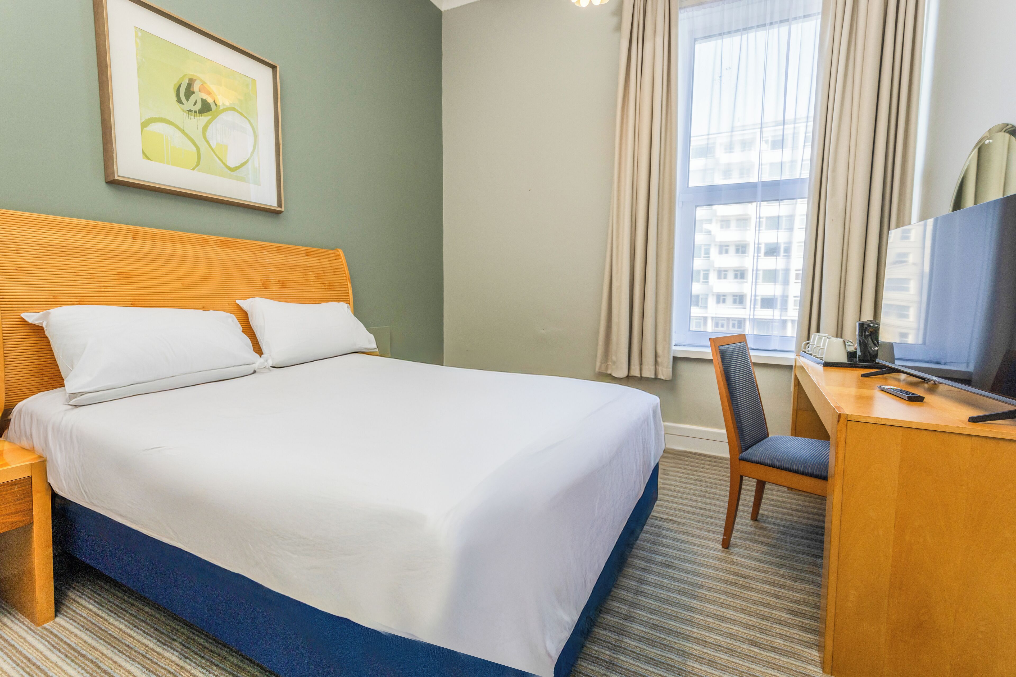 A hotel room with a bed, a desk, a chair, a television, and a window with curtains.