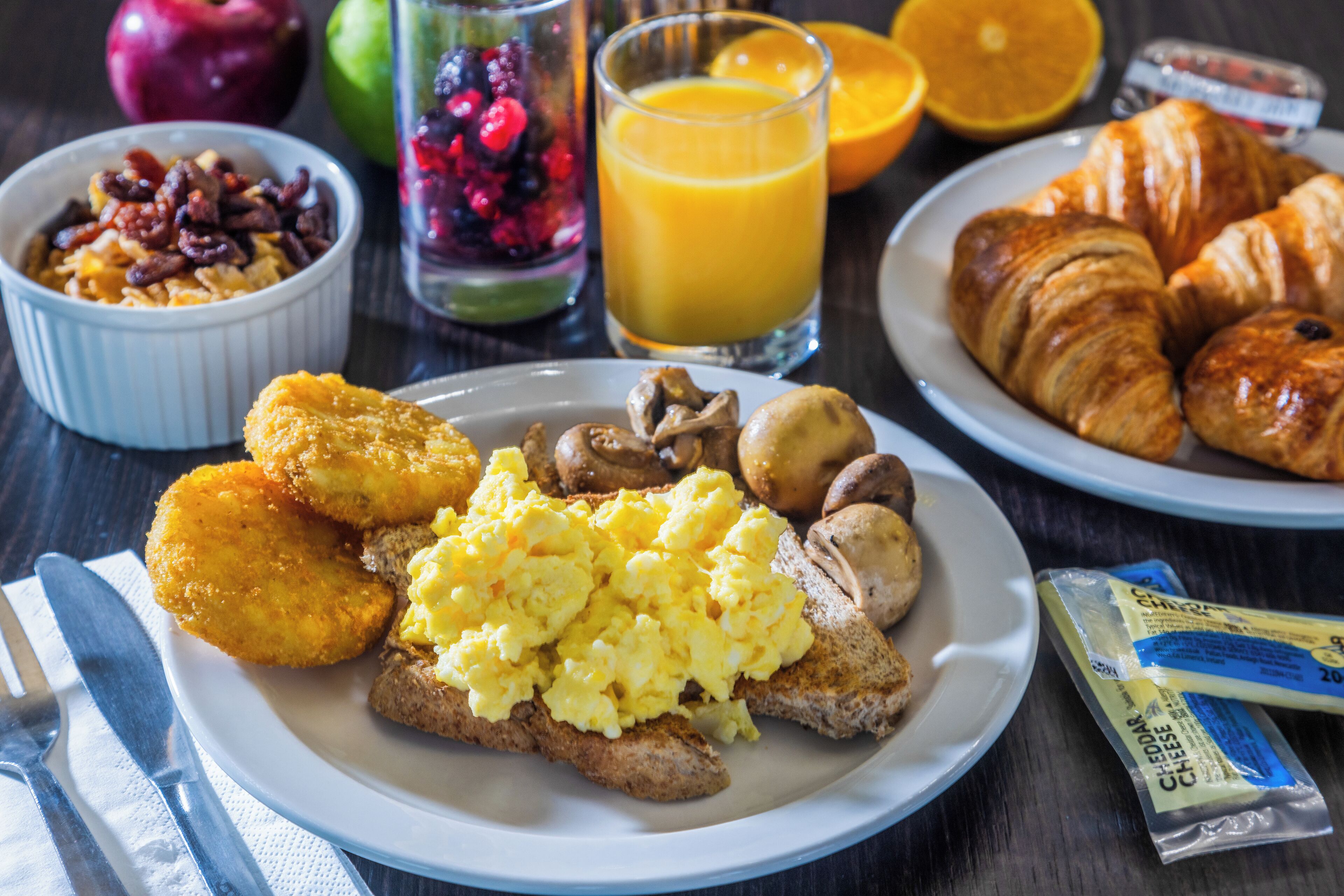 A breakfast plate with scrambled eggs, toast, mushrooms, and croissants.