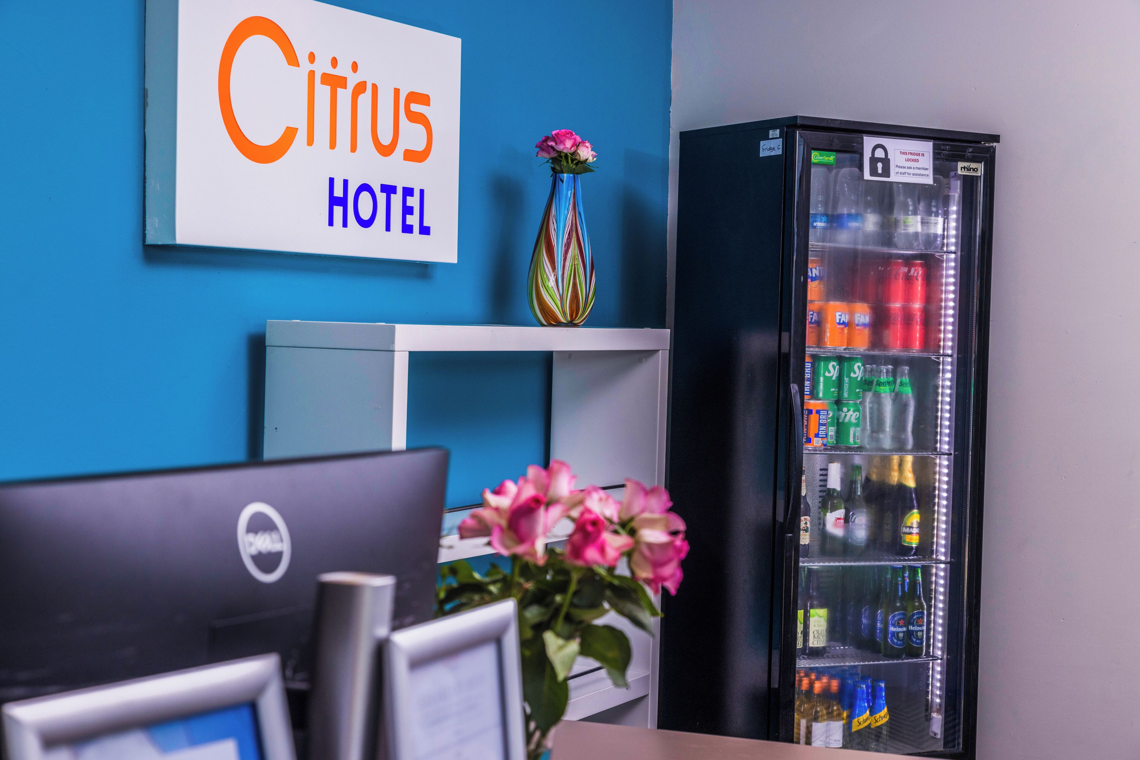 Zona de recepción de un hotel con una computadora, un refrigerador lleno de bebidas y un letrero que dice "Citrus Hotel".