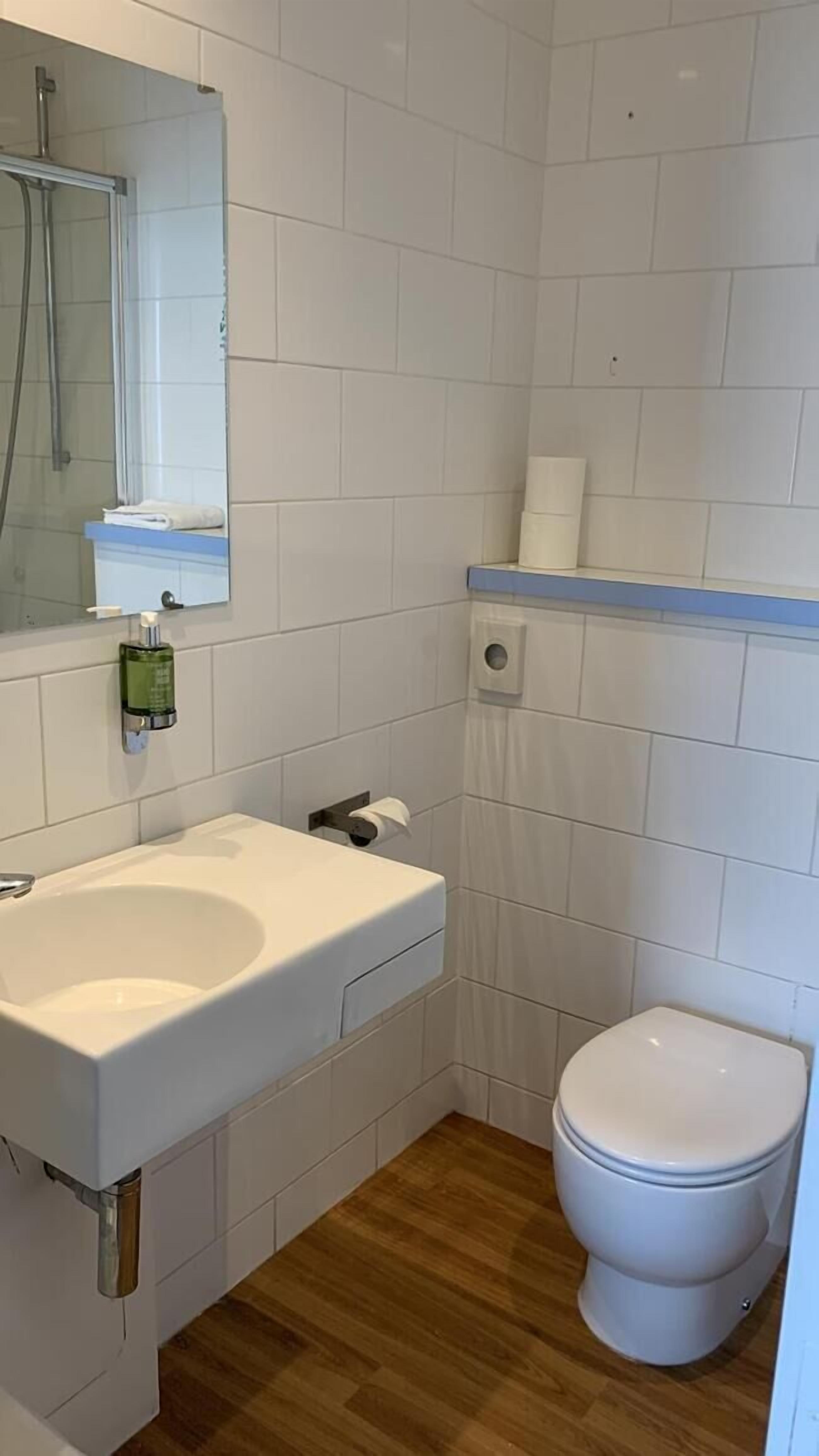 A small, clean bathroom with white tiles, a white sink, a toilet, and a mirror.