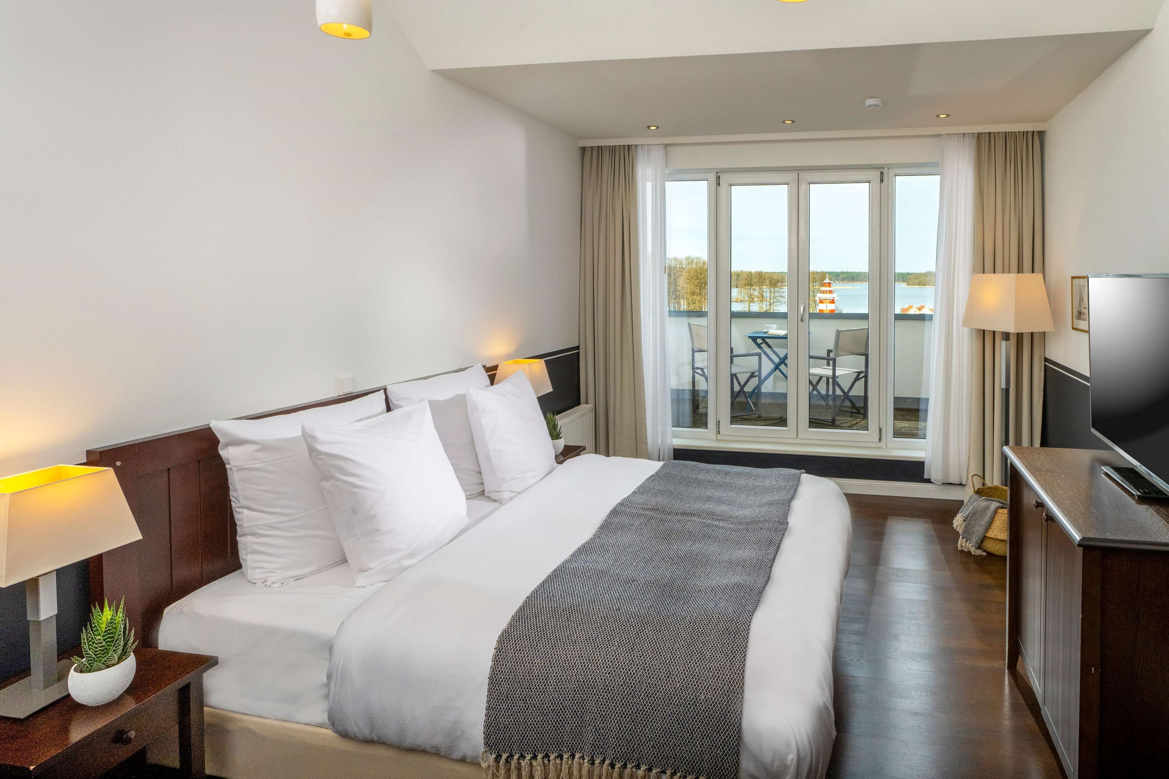 A hotel room with a large bed, two bedside lamps, a TV, and a view of the outside balcony.