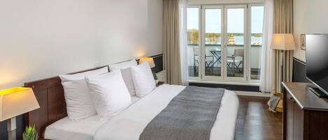 A hotel room with a large bed, two bedside lamps, a TV, and a view of the outside balcony.