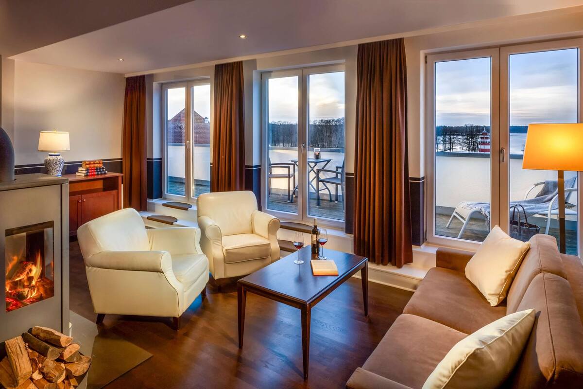 Une chambre d’hôtel moderne dotée d’une cheminée, d’un coin salon et de grandes fenêtres offrant une vue sur l’extérieur.