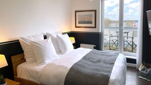A hotel room with a bed, a window with a view of a water body, and a table with chairs outside. - Sunday Resort Hafendorf Rheinsberg (Rheinsberg)