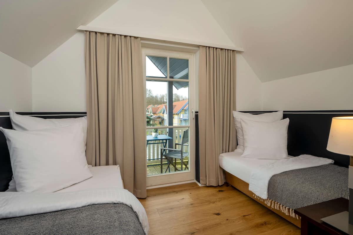 Une chambre d’hôtel avec deux lits, un balcon avec une table et des chaises, et une vue sur les maisons environnantes.
