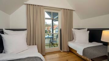 Une chambre d’hôtel avec deux lits, un balcon avec une table et des chaises, et une vue sur les maisons environnantes.