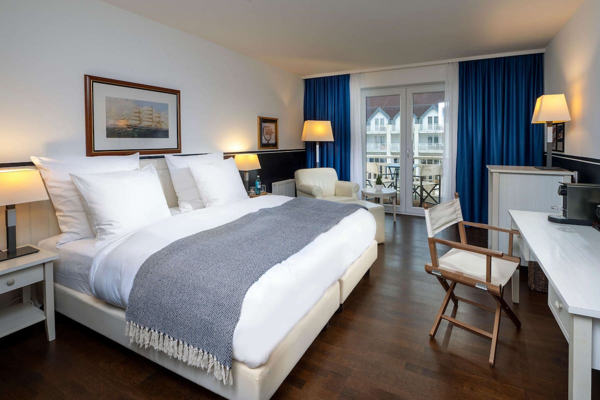 Une chambre d’hôtel avec un grand lit, un bureau, une chaise et un balcon agrémenté de rideaux bleus.