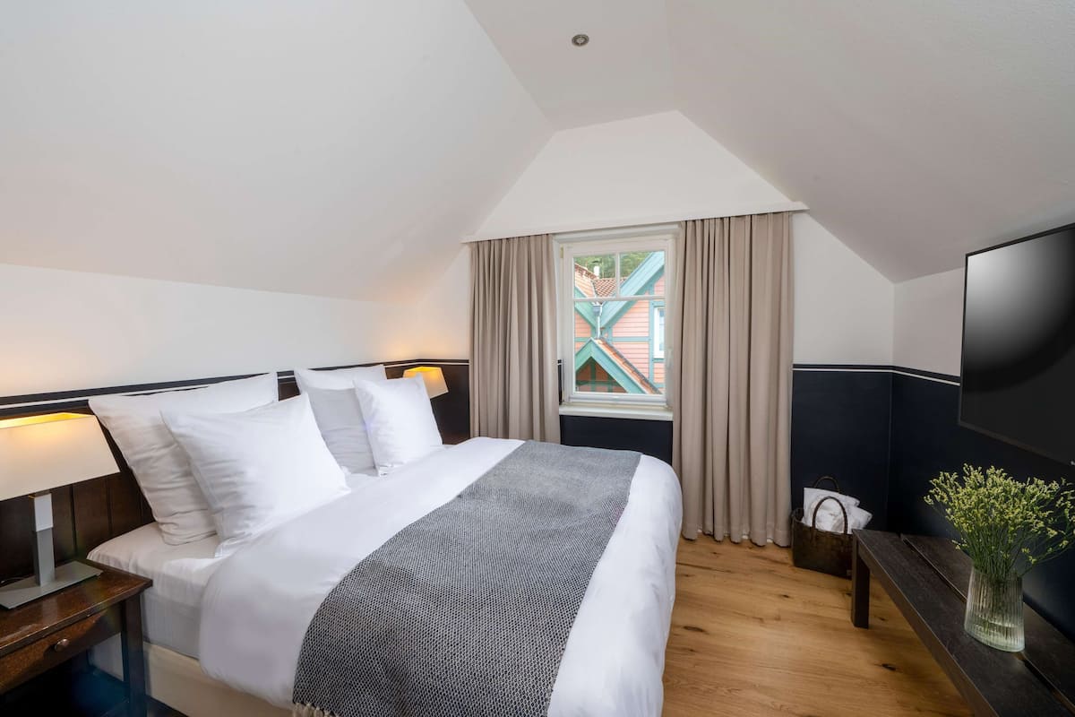 Une chambre d’hôtel avec un lit, une table de chevet, une lampe, une télévision et une fenêtre avec des rideaux.