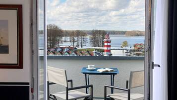 Een balkon met een tafel en twee stoelen, met uitzicht op een meer met huizen en een vuurtoren.