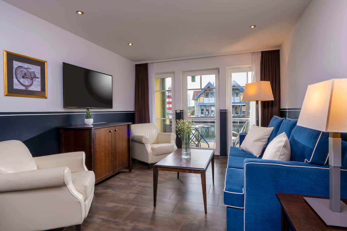 Une chambre d’hôtel moderne dotée d’une télévision à écran plat, d’un canapé, d’un fauteuil, d’une armoire en bois et offrant une vue sur les bâtiments colorés de la ville.