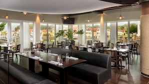 A restaurant with large windows, wooden tables, and black leather seating. - Sunday Resort Hafendorf Rheinsberg (Rheinsberg)