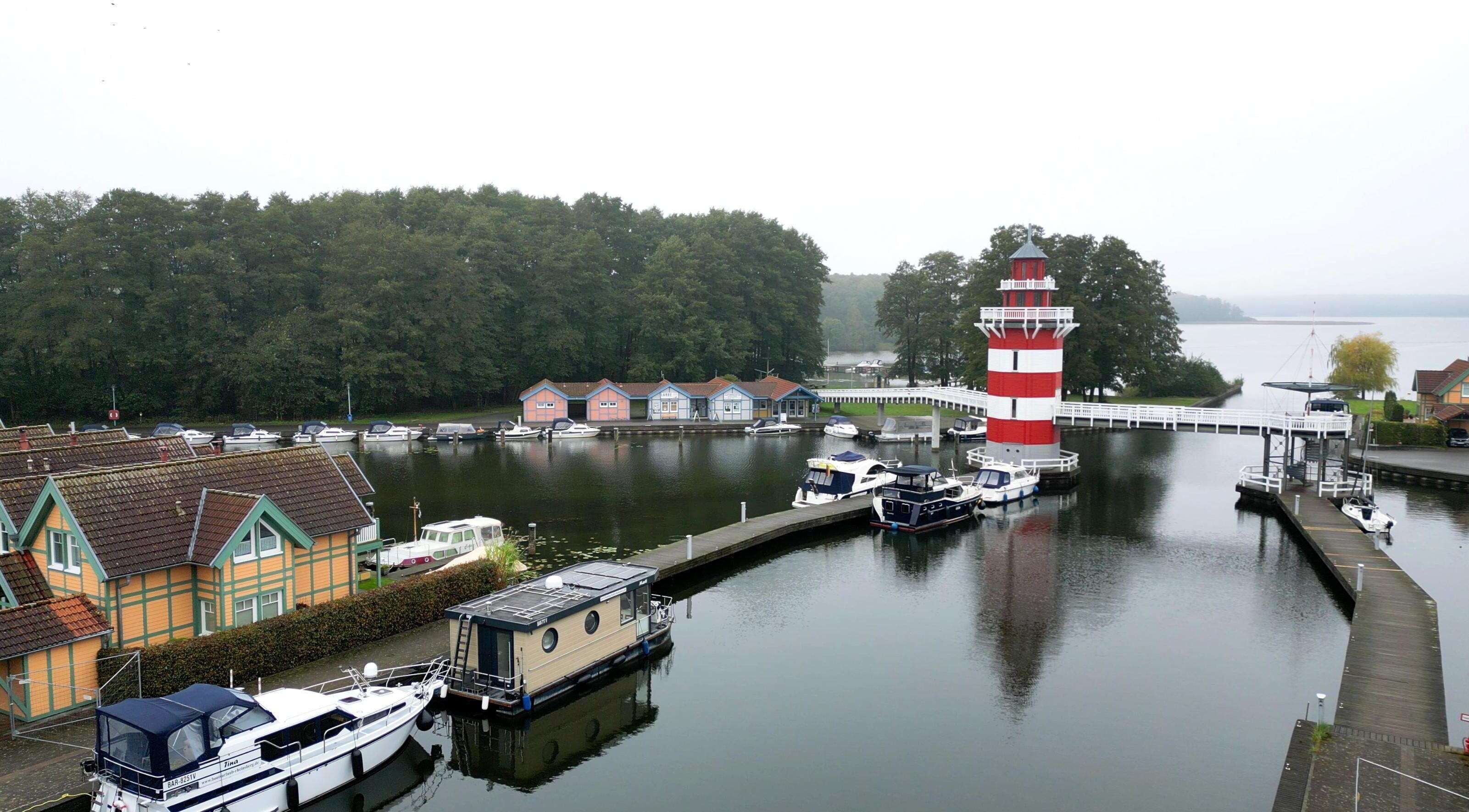A harbor with boats docked, a lighthouse, and a row of houses along the water.