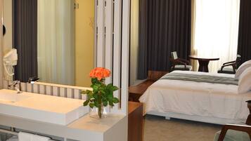 Ein modernes Hotelzimmer mit einem großen Bett, einem eigenen Badezimmer mit Waschtisch sowie einer Sitzecke mit zwei Stühlen und einem Tisch.