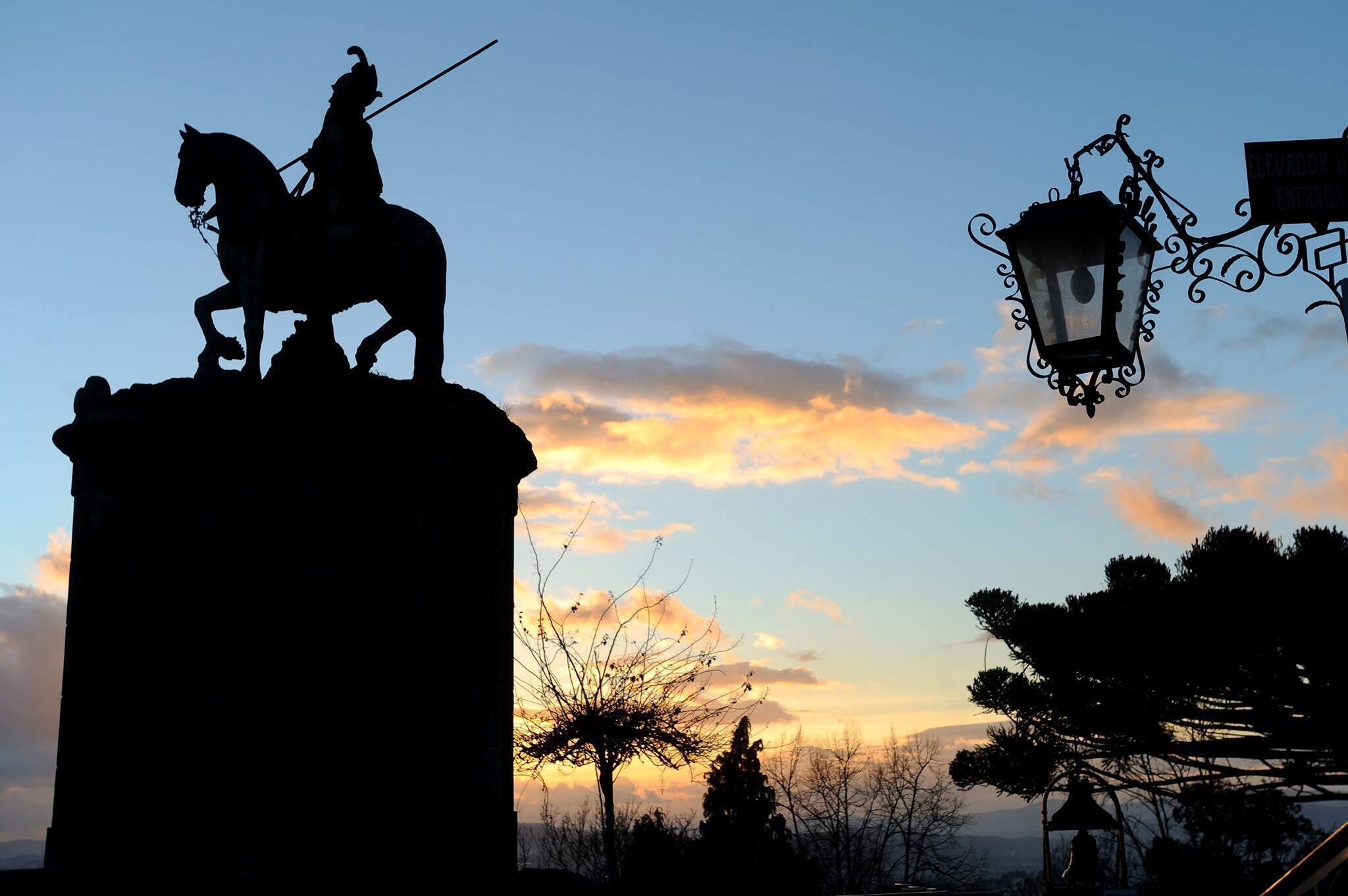 La silhouette d’une statue, posée sur un piédestal, se détache sur le ciel au coucher du soleil.