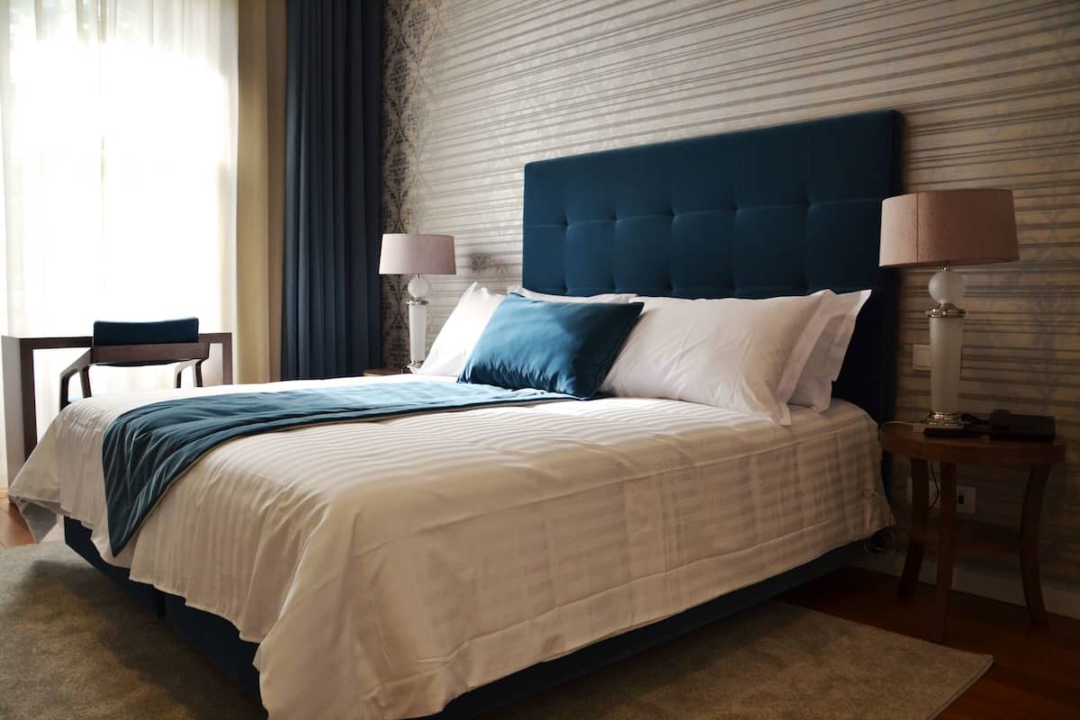 A neatly made bed with a blue headboard, white bedding, and a blue throw blanket. There are two bedside tables with lamps.