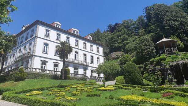 A large white building with multiple windows and a balcony, surrounded by well-maintained gardens and a gazebo. - Hotel do Parque (Braga)