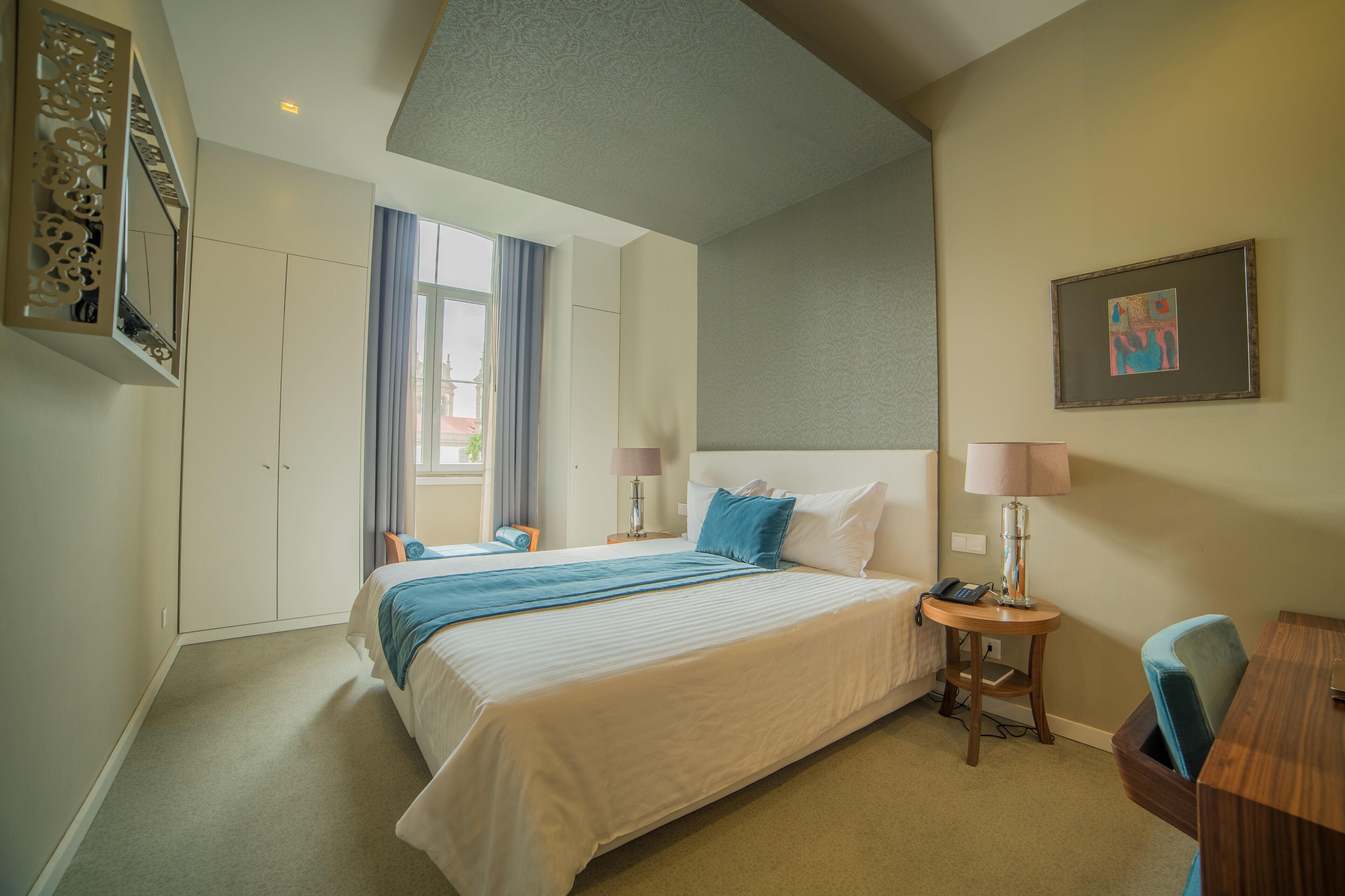 Habitación de hotel con una cama grande, un escritorio, una silla, una lámpara, un teléfono y una ventana con cortinas.