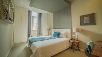 Habitación de hotel con una cama grande, un escritorio, una silla, una lámpara, un teléfono y una ventana con cortinas.