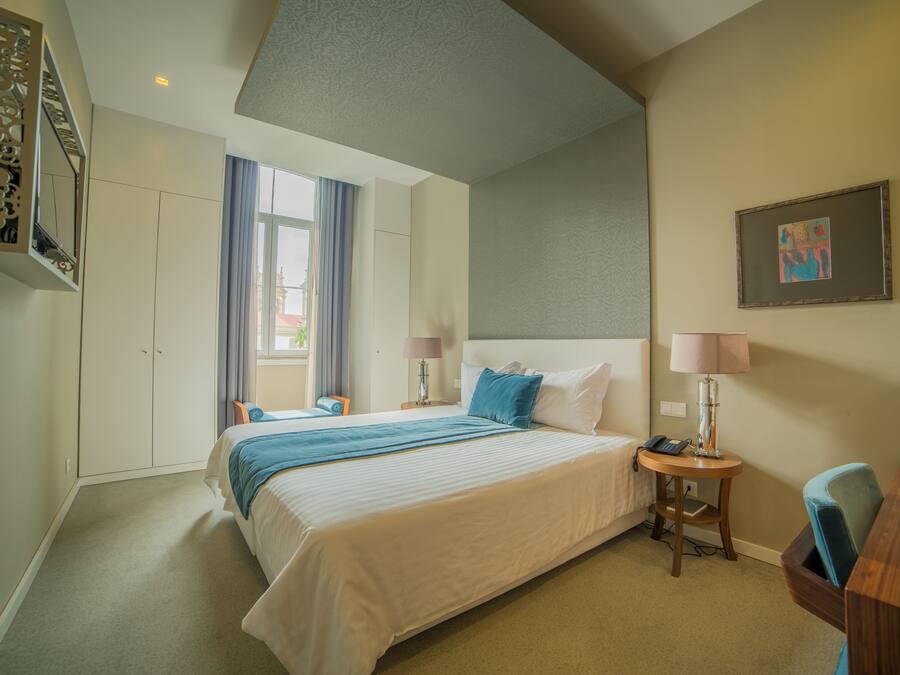Habitación de hotel con una cama grande, un escritorio, una silla, una lámpara, un teléfono y una ventana con cortinas.