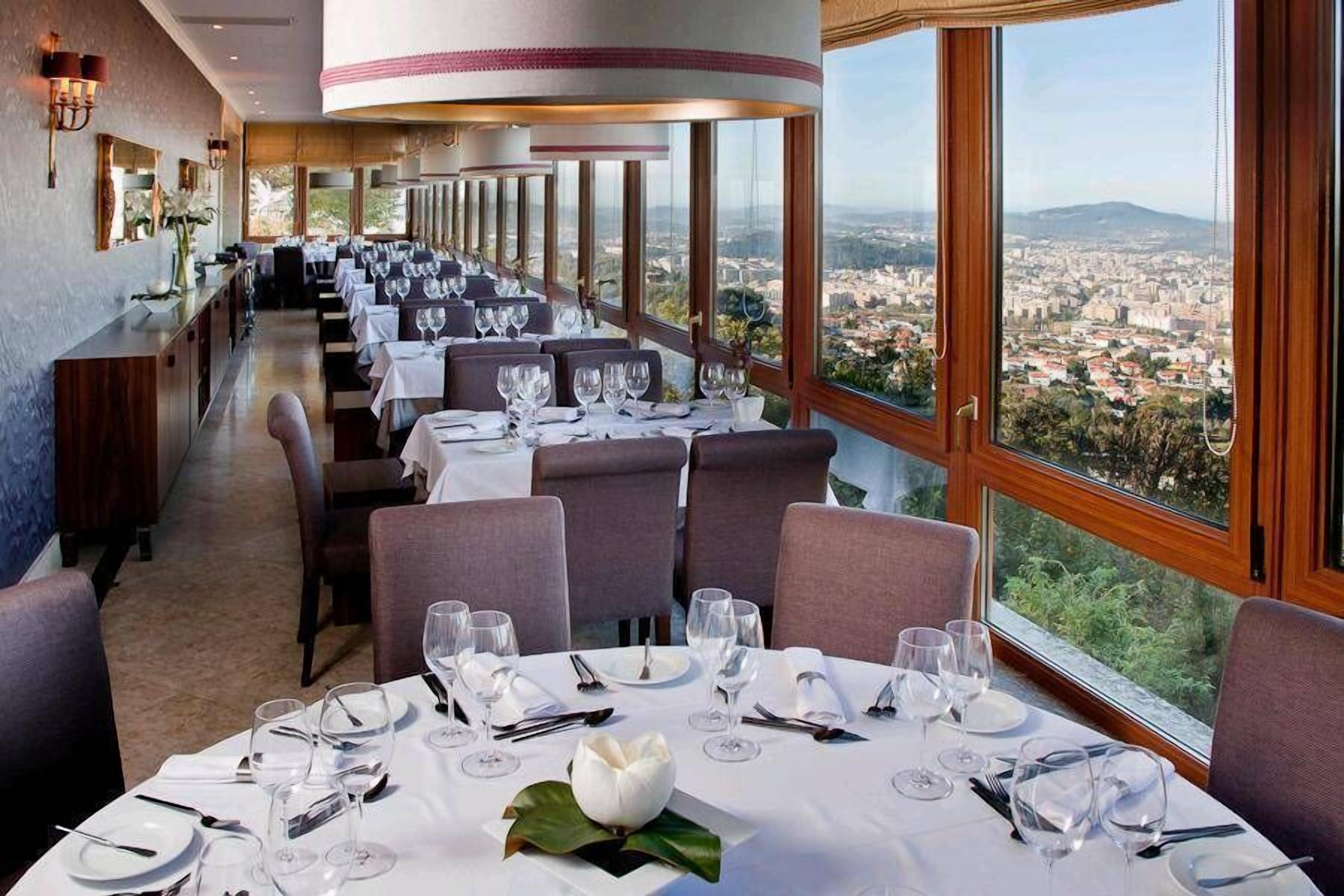 Ein Restaurant mit gedeckten Tischen, großen Fenstern mit Blick auf die Stadt und einem modernen Interieur.