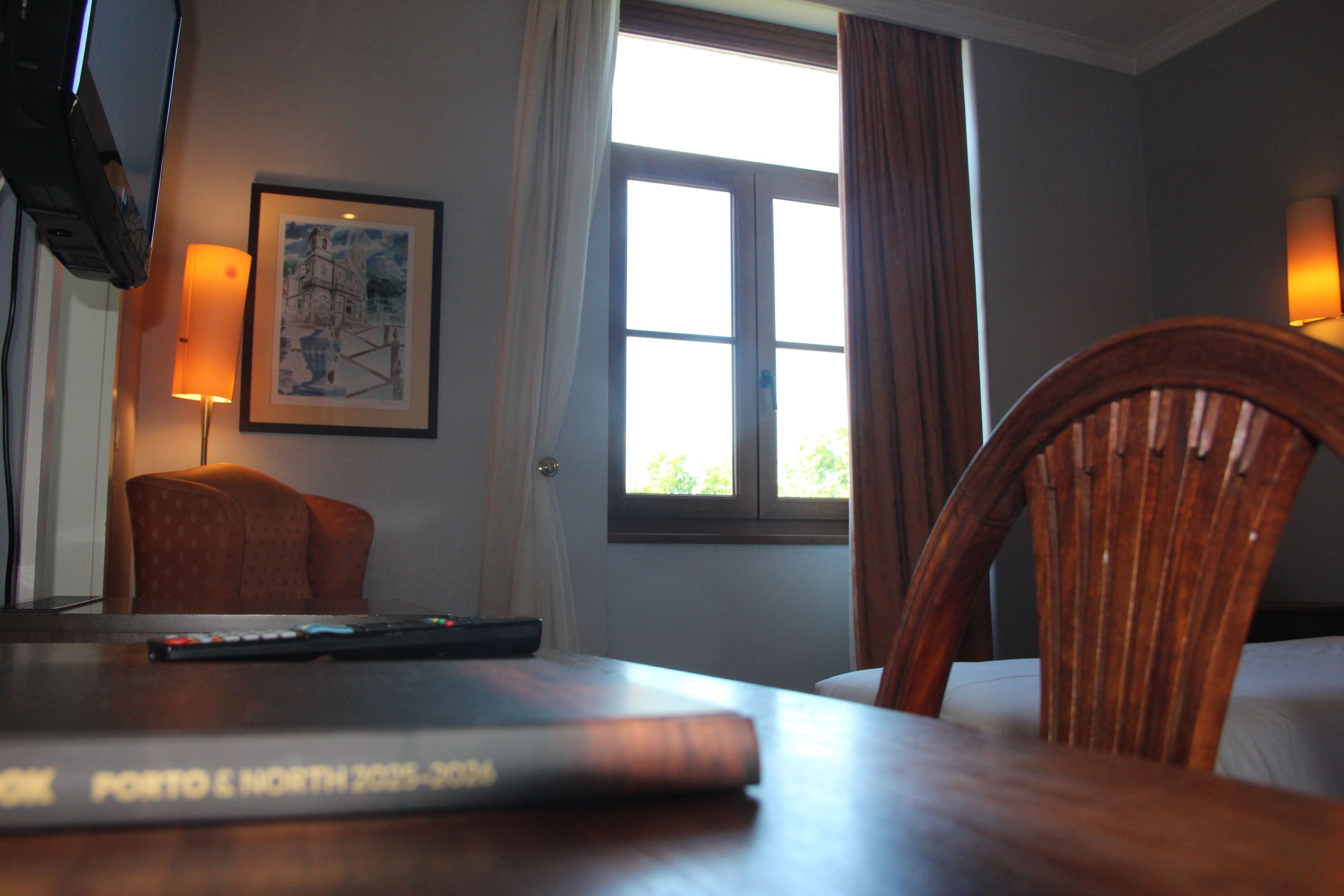A hotel room with a bed, a chair, a table with a remote control, a lamp, and a framed picture on the wall.