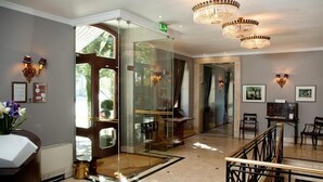 A hotel lobby with a reception desk, a glass elevator, chandeliers, framed pictures on the walls, and a staircase. - Hotel do Elevador (Braga)