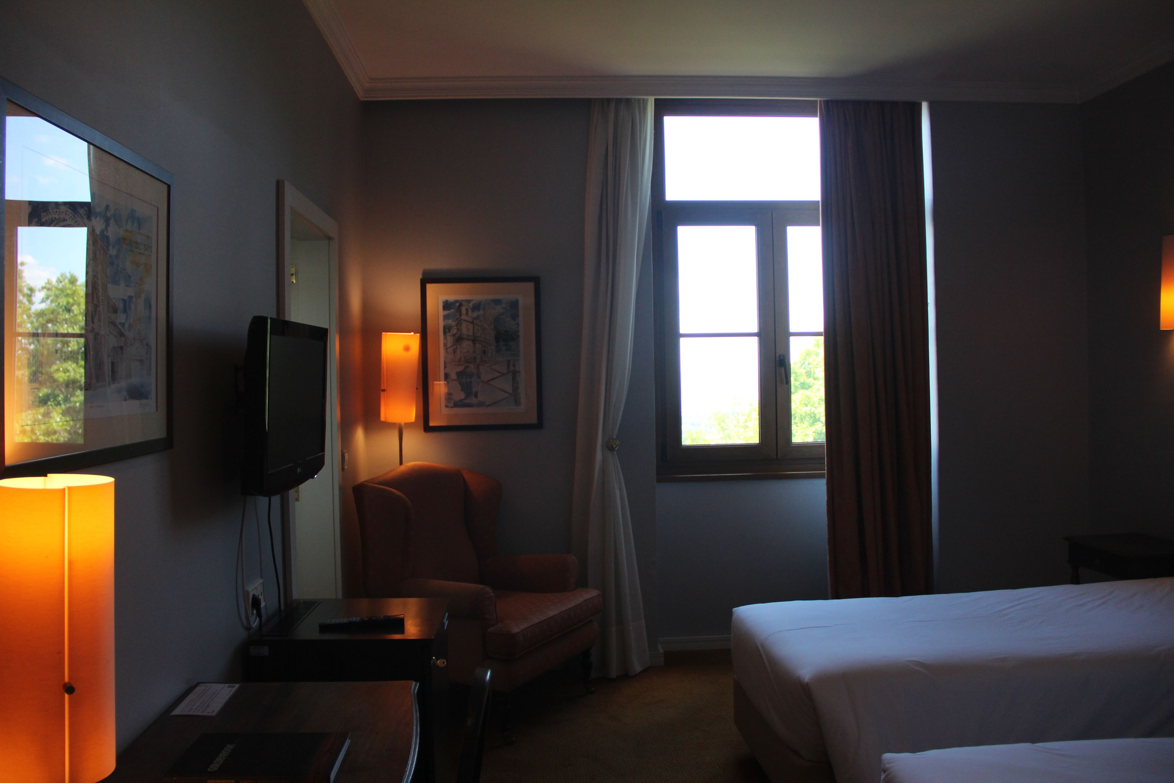 Een hotelkamer met een bed, een bureau met een lamp, een stoel, een televisie en een raam met gordijnen.