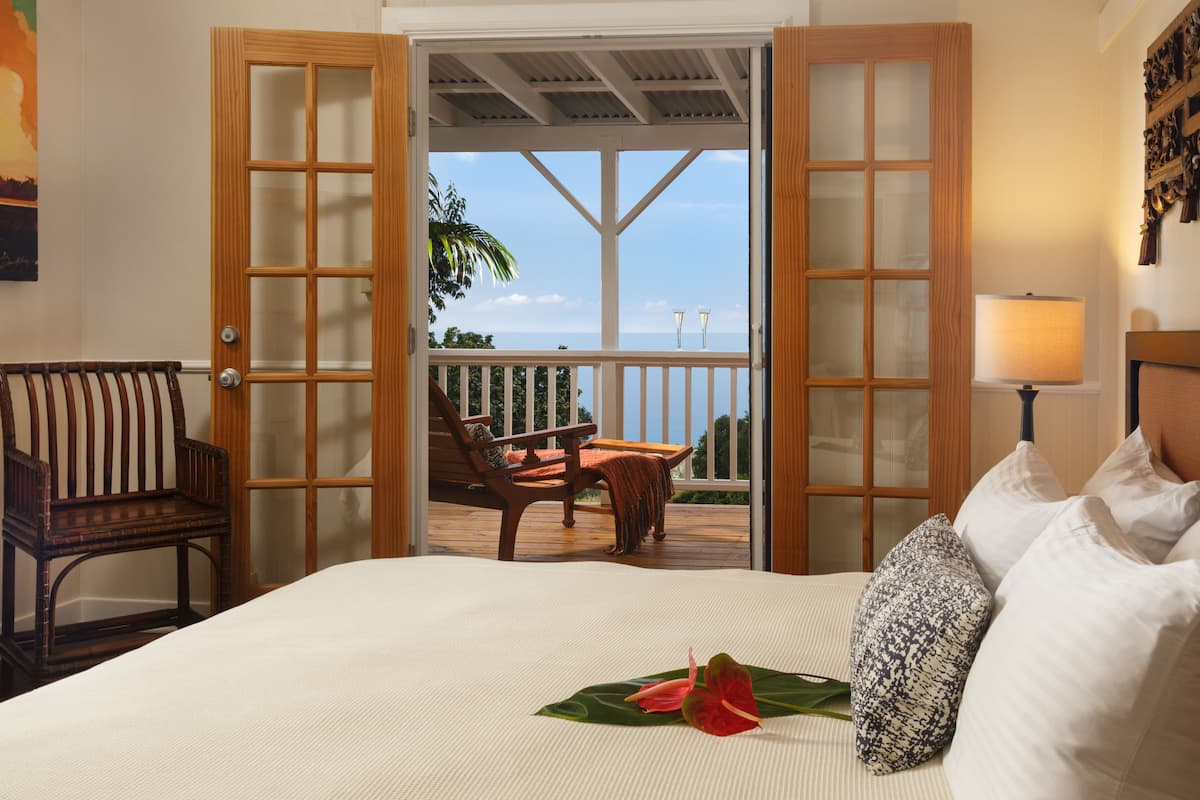 A hotel room with a bed, a chair, a table, and a balcony with a view of the ocean.