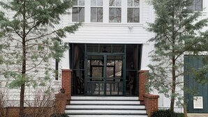 A two-story building with a front entrance featuring a set of steps leading to a glass door. - Cameron House Inn (Manteo)