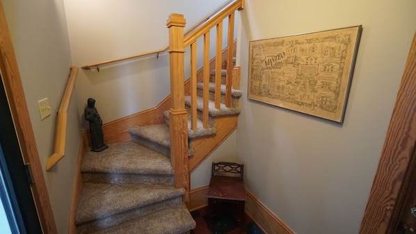 A wooden staircase with carpeted steps and a handrail, leading to a landing with a framed map.
