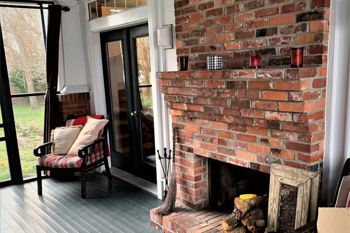 A cozy room with a brick fireplace, a comfortable chair, a rug, and a view through a glass door.