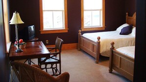 A bedroom with a bed, two windows, a desk with a lamp, and a chair. - Cameron House Inn (Manteo)