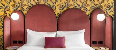 Una habitación de hotel con cama, mesita de noche, lámpara de lectura y un muro decorado con un diseño de hojas.