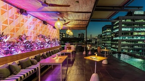A rooftop bar with seating, a pool, and city views at dusk.